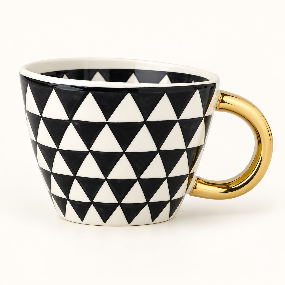 A ceramic coffee mug featuring a black and white geometric triangle pattern and a polished gold handle, shown on a clean white background.