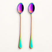 Two long spoons with an iridescent rainbow finish, standing upright against a clean off-white background.