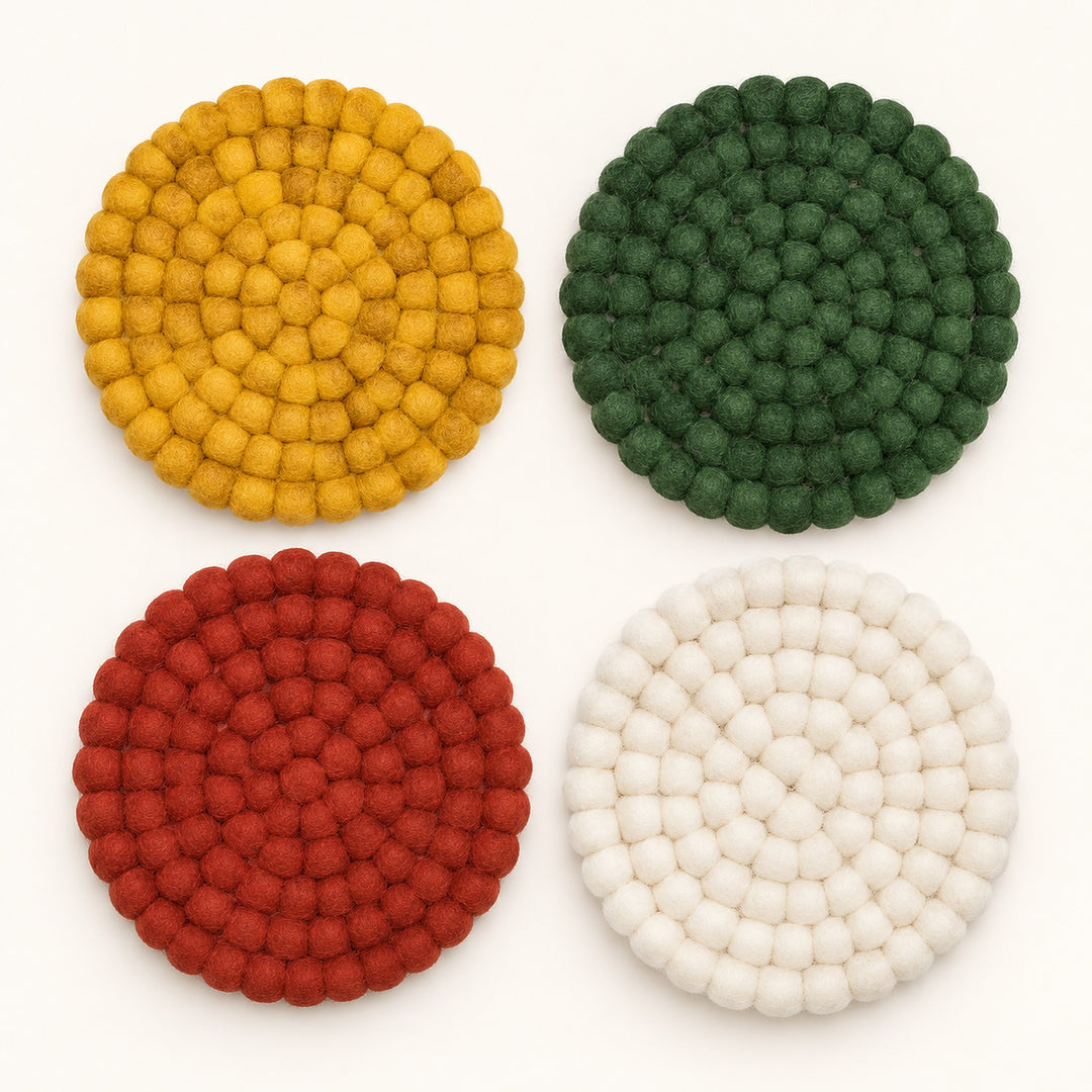 Four round felt pom-pom coasters arranged in a 2x2 grid on a white background, featuring yellow, green, red, and off-white colors.