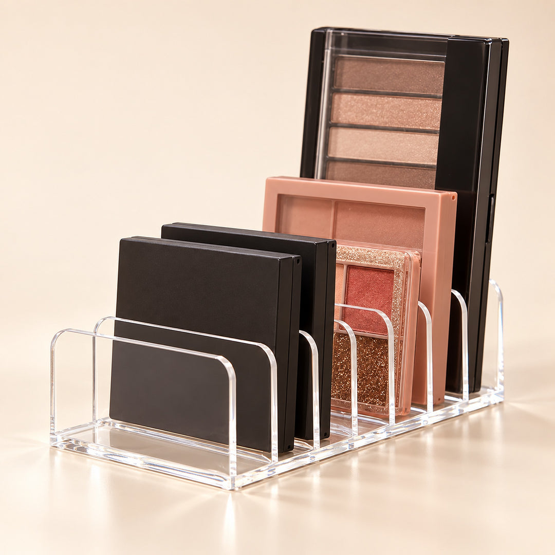 Clear acrylic makeup organizer stand holding several eyeshadow palettes in black and warm neutral shades against a soft beige studio background.