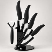 A black kitchen knife set with matching black-handled tools, including knives and a peeler, displayed on a round stand against a light gray background.