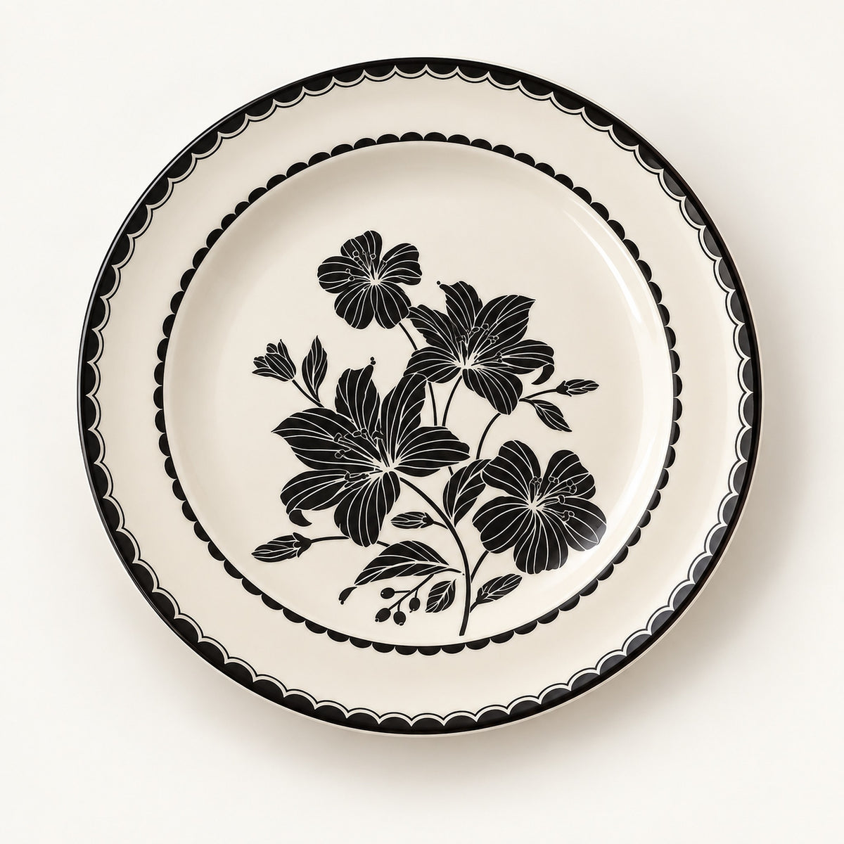 A round ceramic plate with a cream-colored glaze, featuring a black floral pattern in the center and a decorative black scalloped border around the rim, shown against a plain off-white background.