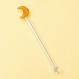 One amber Moon glass stirrer, approximately 12.5 cm long, on pale yellow studio background.