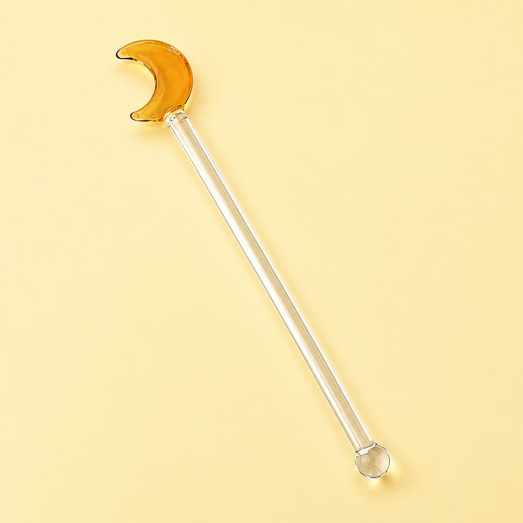 One amber Moon glass stirrer, approximately 12.5 cm long, on pale yellow studio background.