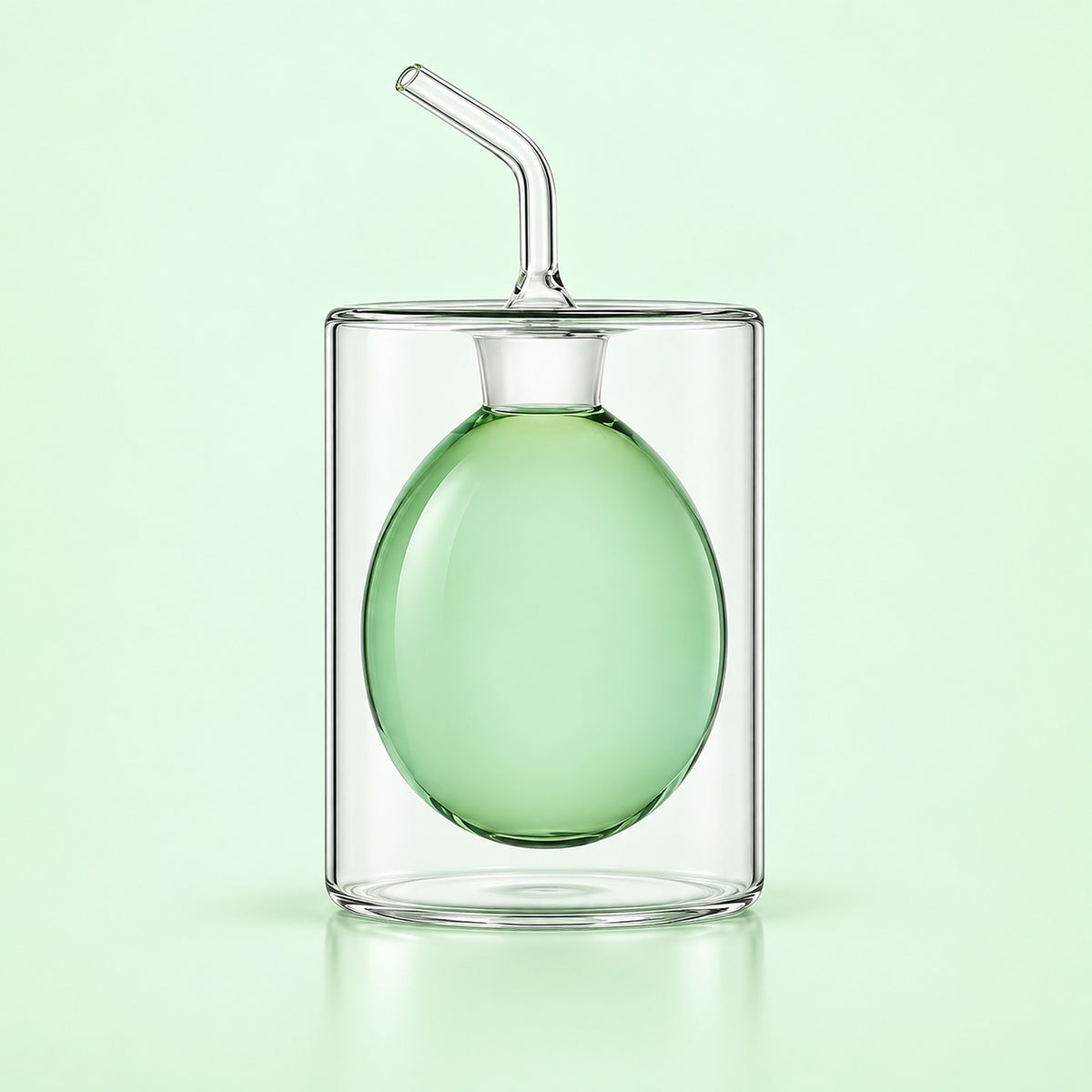A clear glass double-walled cup with a matching clear glass straw, featuring a translucent light green inner balloon or sphere, set against a solid pale green background.