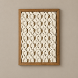 A square framed wall art piece featuring a cream crocheted or knitted floral pattern set within a medium brown wooden frame, mounted on a warm beige wall.
