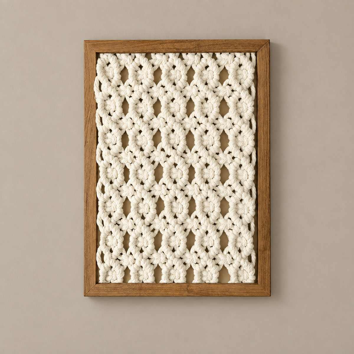 A square framed wall art piece featuring a cream crocheted or knitted floral pattern set within a medium brown wooden frame, mounted on a warm beige wall.