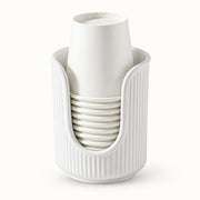 A white ribbed cup holder cradling a stack of white paper cups, photographed against a seamless white background.
