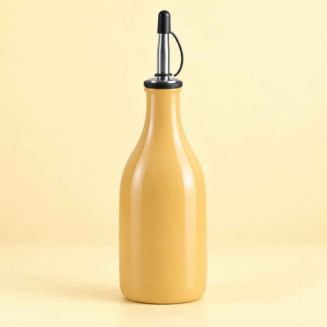 A glossy mustard-yellow glass bottle with a black and stainless steel pour spout, set against a solid pale yellow background.