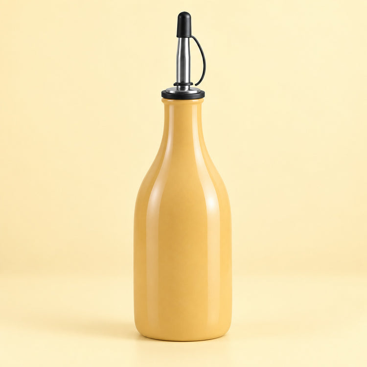 A glossy mustard-yellow glass bottle with a black and stainless steel pour spout, set against a solid pale yellow background.