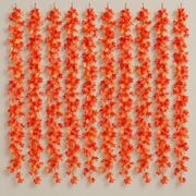 Ten artificial maple leaf garland strands hung side by side on a warm neutral wall