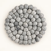 A round, handmade felt pouf coaster or trivet made of layered gray and white wool loops, photographed from directly above on a clean off-white background.