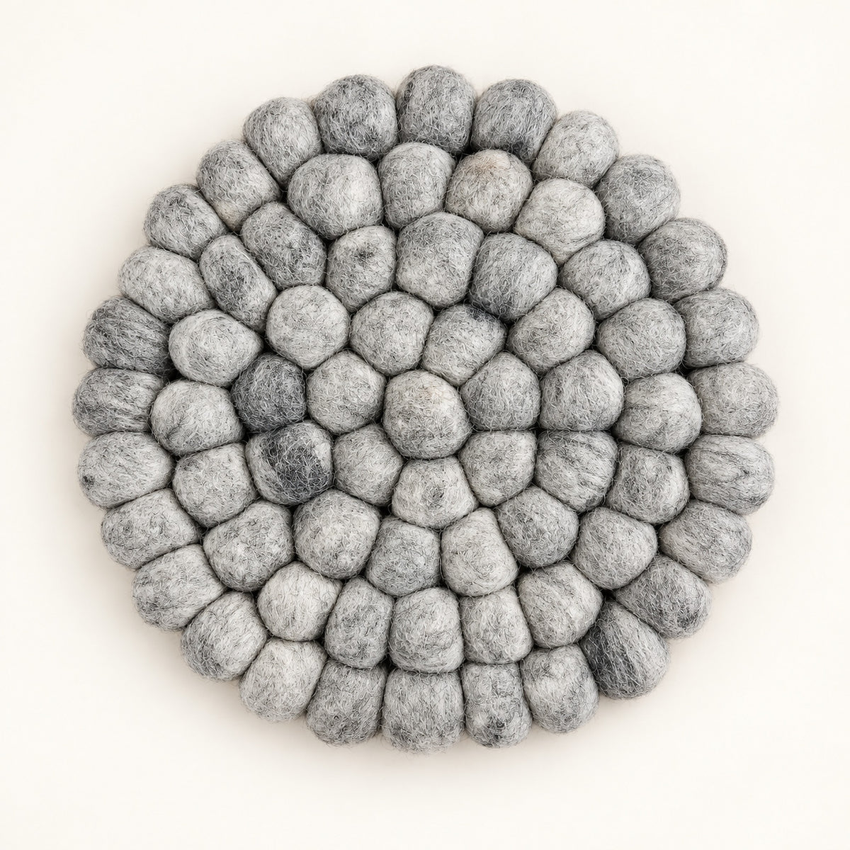 A round, handmade felt pouf coaster or trivet made of layered gray and white wool loops, photographed from directly above on a clean off-white background.