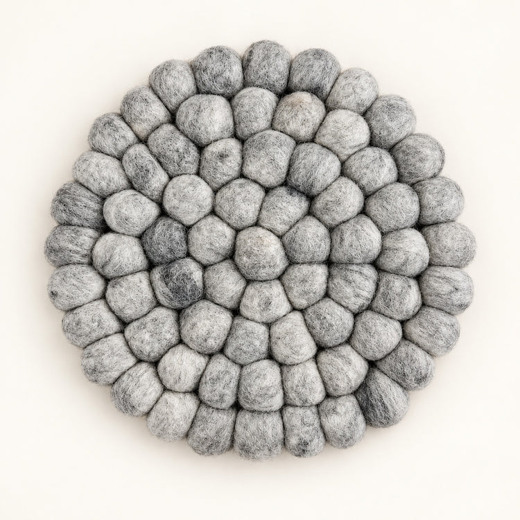 A round, handmade felt pouf coaster or trivet made of layered gray and white wool loops, photographed from directly above on a clean off-white background.