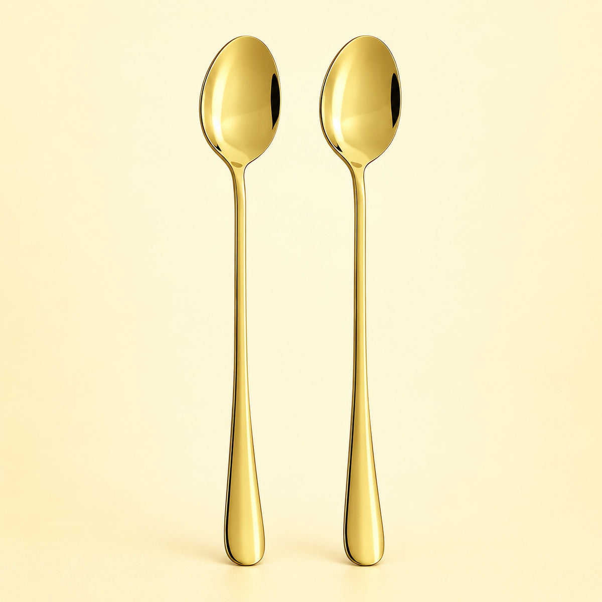 Two slim gold spoons standing upright side by side on a warm cream background.