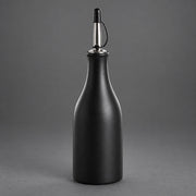 A matte black bottle with a metallic silver and black pour spout, set against a solid gray studio background.
