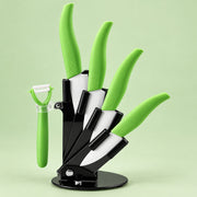 A kitchen utensil set with bright green handles, including four knives and a peeler, displayed on a black stand against a pale green background.