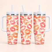 Three handled insulated tumblers with white straws, shown from front and side angles. The tumblers have a repeating lip-print pattern in coral pink, orange, and red on a warm off-white background.