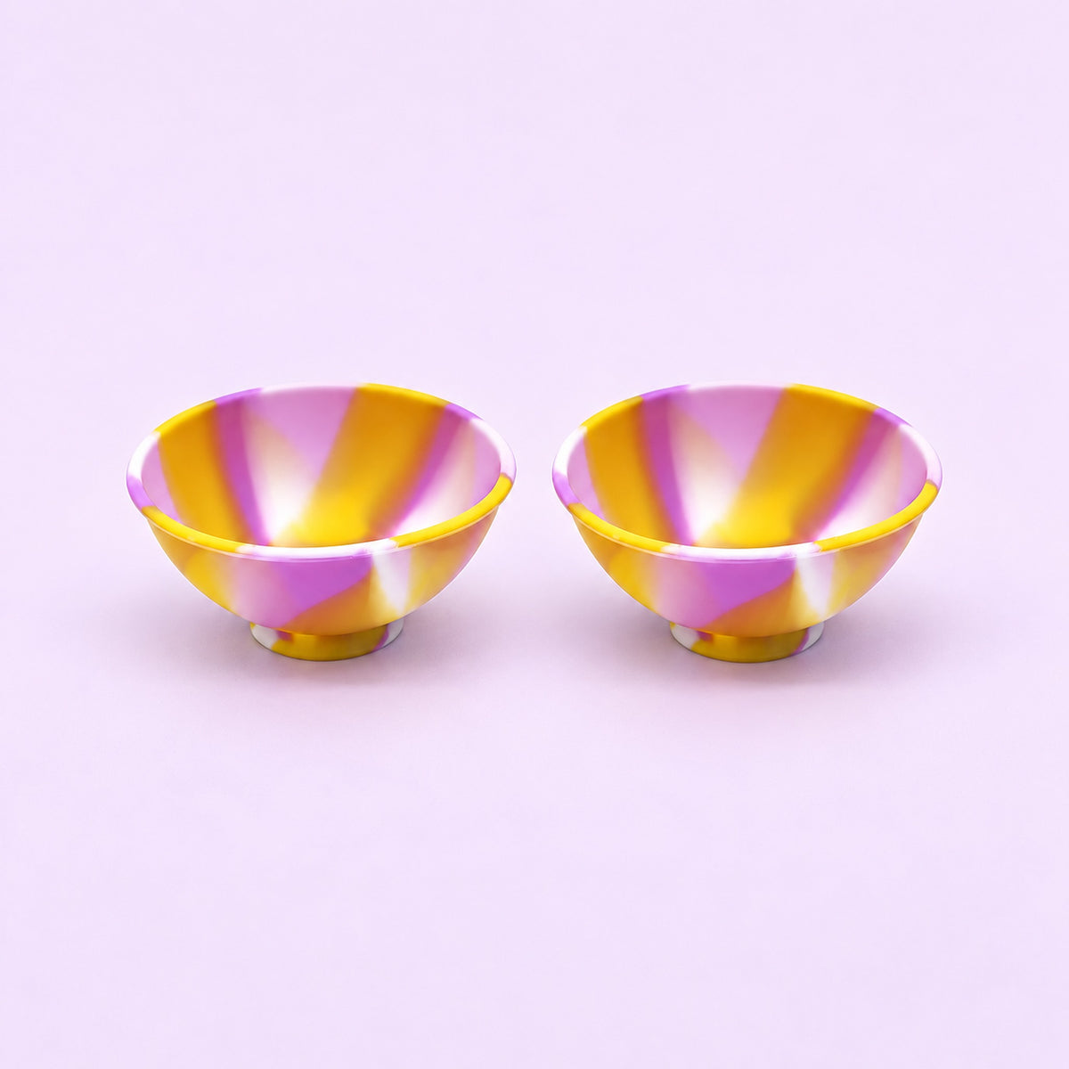 Two yellow purple and white swirl silicone mini bowls, open tops and pedestal bases.