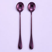 Two long-handled spoons with a glossy metallic purple finish, arranged vertically side-by-side on a light lavender background.