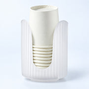 A stack of off-white paper cups held upright in a translucent white plastic cup holder with vertical ridges, photographed on a clean light blue studio background.