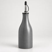 A matte gray ceramic bottle with a pour spout featuring a black plastic cap and a silver metal loop handle, set against a plain light gray background.