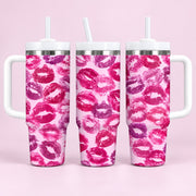 Three handled stainless steel tumblers with white straws, featuring a repeating pink and purple lip print pattern on a light pink background, set against a solid light pink backdrop.