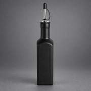A matte black rectangular bottle with a pour spout, shown centered against a neutral gray studio background.
