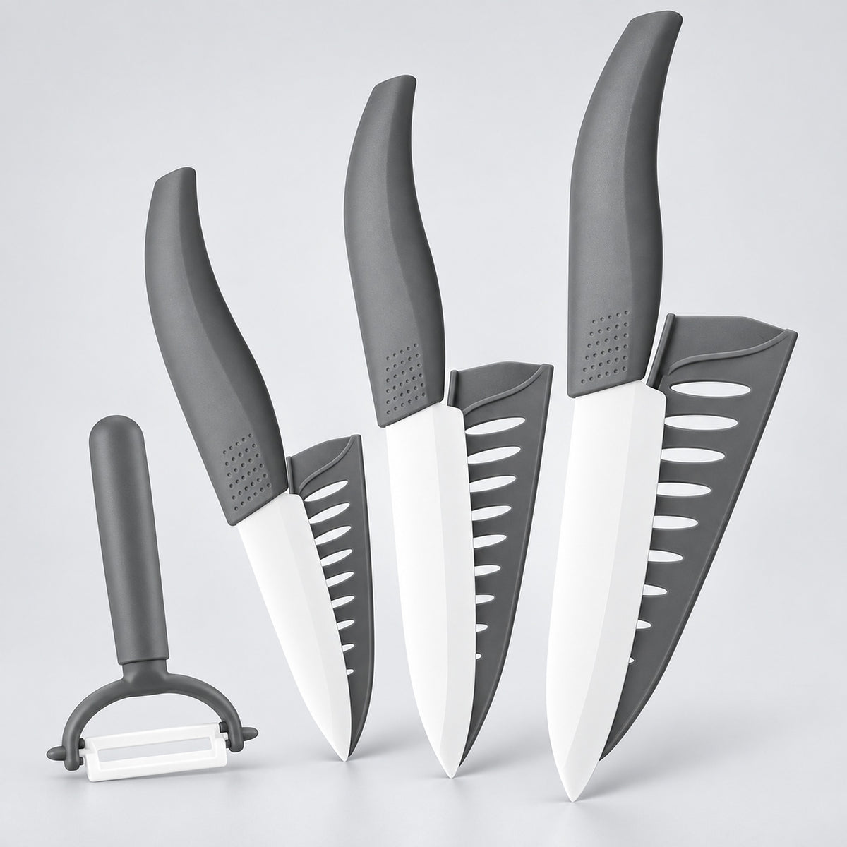 Four kitchen knives and a peeler with dark gray handles and white blades, arranged upright on a light gray studio background.