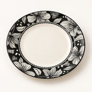 An oval ceramic plate with a black and white floral patterned rim and a solid white center, photographed from directly above on a light off-white background.