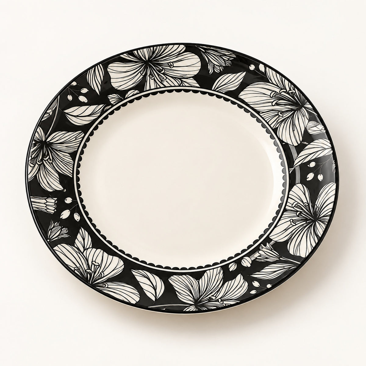 An oval ceramic plate with a black and white floral patterned rim and a solid white center, photographed from directly above on a light off-white background.