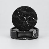 A set of black marble coasters, with one round coaster leaning against a stack of rectangular coasters on a light gray background.