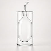 Clear glass double-walled tumbler with an integrated oval-shaped glass insert and a small angled glass pour spout on top, shown on a light gray studio background.