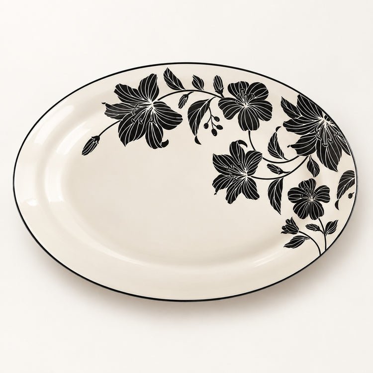 An oval ceramic serving platter with a glossy white background and a black floral vine pattern along the right side and rim, set against a clean white background.