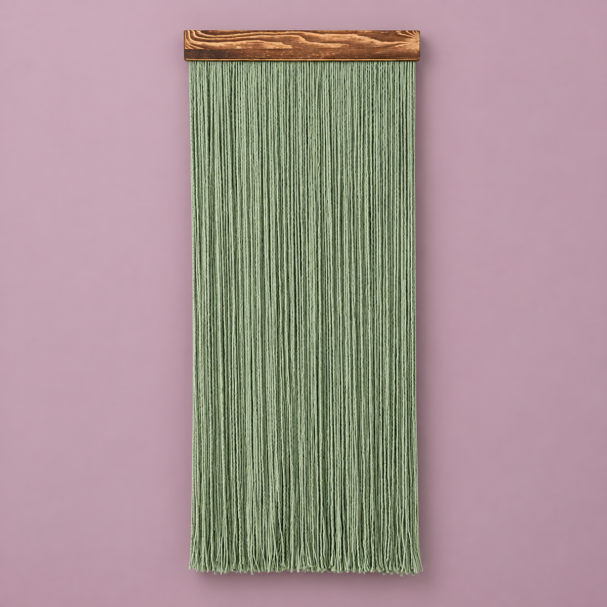 A vertical sage green macrame wall hanging with a natural wood dowel, displayed against a solid dusty pink background.