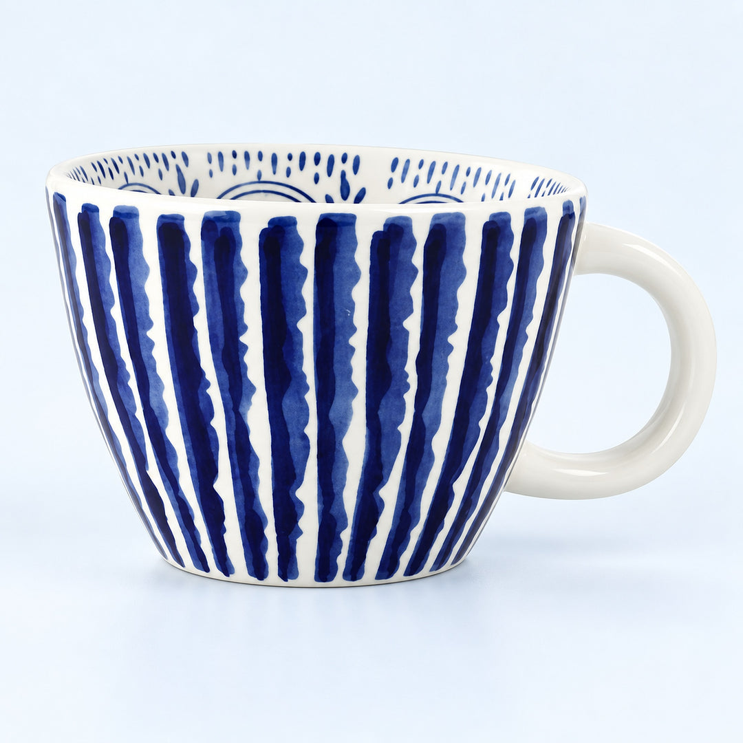 A white ceramic coffee mug with a handle, decorated with vertical navy blue brushstroke stripes and a blue dotted pattern inside, set against a light blue background.