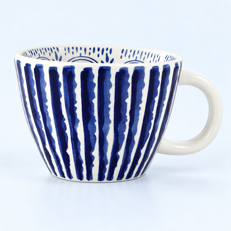 A white ceramic coffee mug with a handle, decorated with vertical navy blue brushstroke stripes and a blue dotted pattern inside, set against a light blue background.