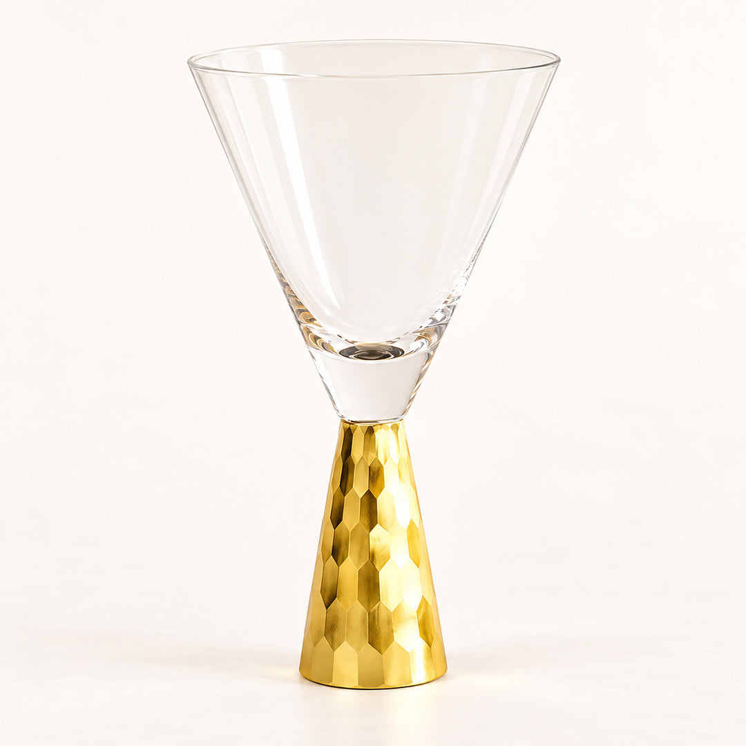A clear glass martini-style coupe glass with a textured metallic gold base, photographed on a clean white studio background.