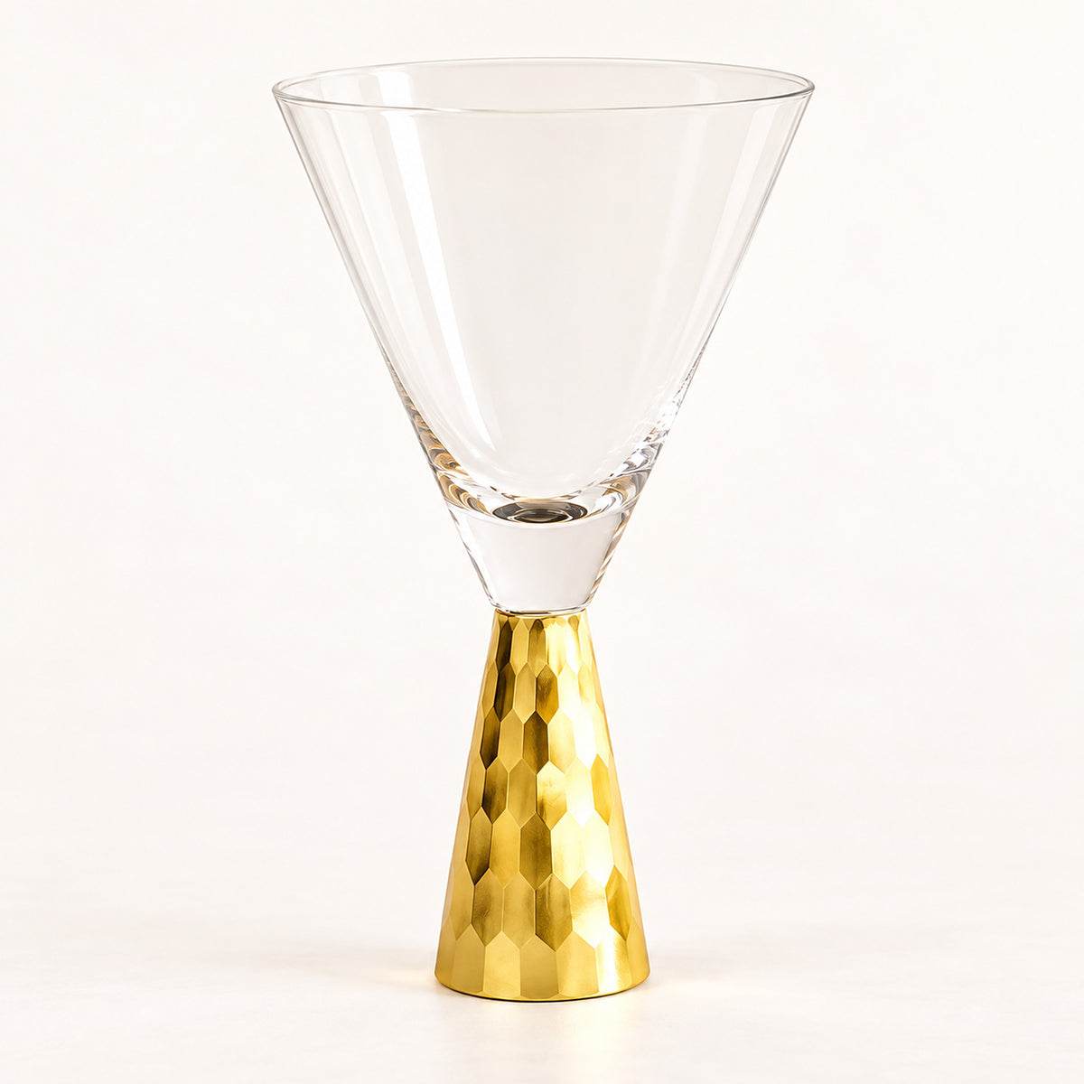 A clear glass martini-style coupe glass with a textured metallic gold base, photographed on a clean white studio background.