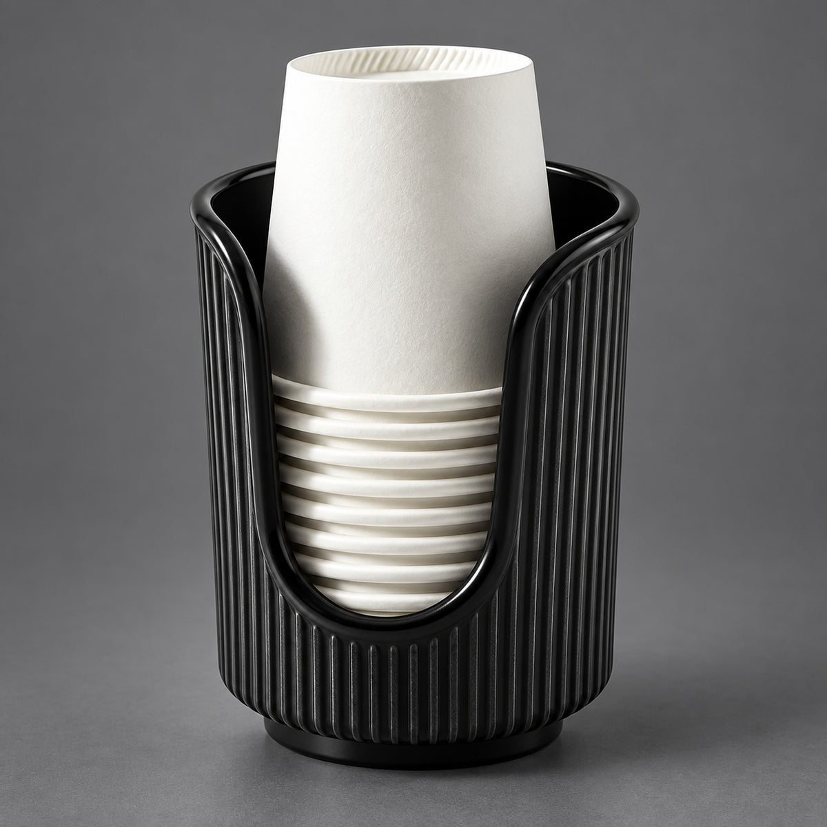 A black ribbed cup holder or cup dispenser holding a stack of white paper cups, photographed on a smooth gray studio background.
