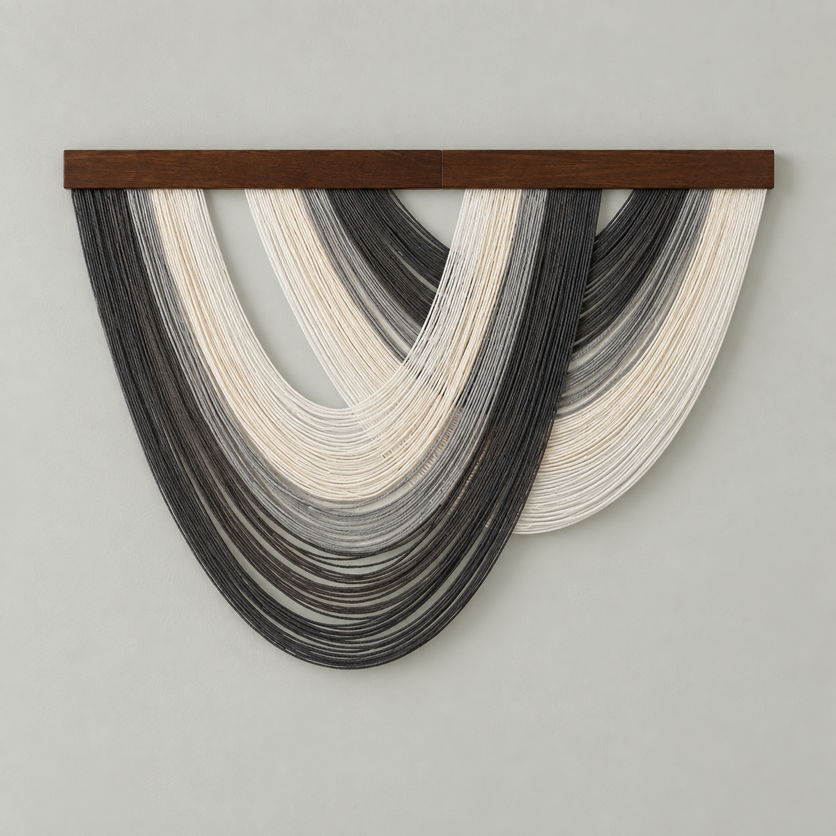A modern wall hanging sculpture featuring layered, semi-circular strands in black, gray, and off-white, suspended from a dark brown wooden bar against a solid light gray wall.