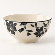 An off-white ceramic bowl featuring a black floral pattern on the exterior and a thin black rim, photographed against a clean white background.