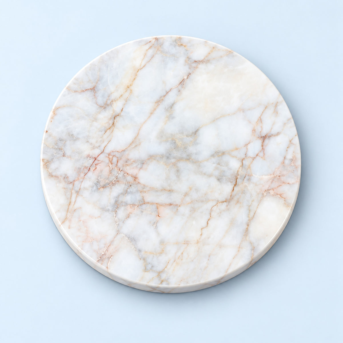 A round white marble board with natural beige and light brown veining, photographed from directly above on a light blue background.