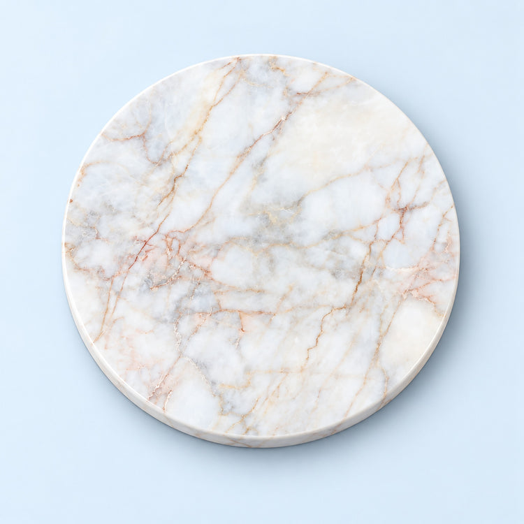 A round white marble board with natural beige and light brown veining, photographed from directly above on a light blue background.