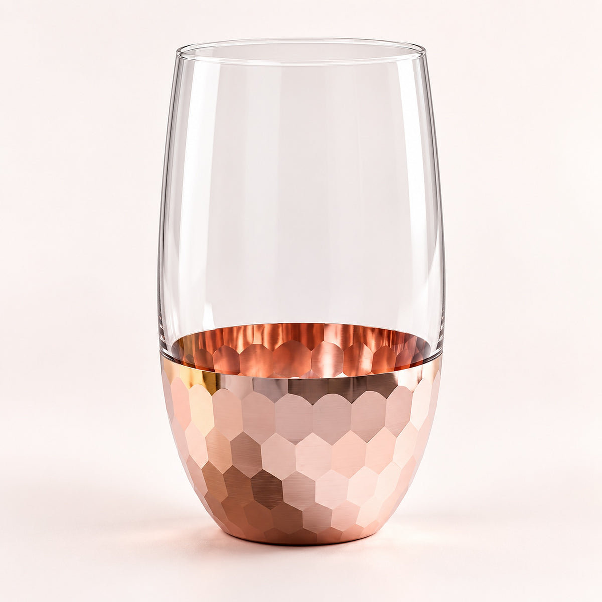 A stemless wine glass with a clear upper half and a hammered metallic rose-gold copper lower half, shown on a clean off-white background.