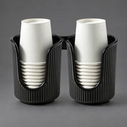 Two black ribbed cup holders, each holding a stack of white paper cups, photographed on a smooth gray studio background.