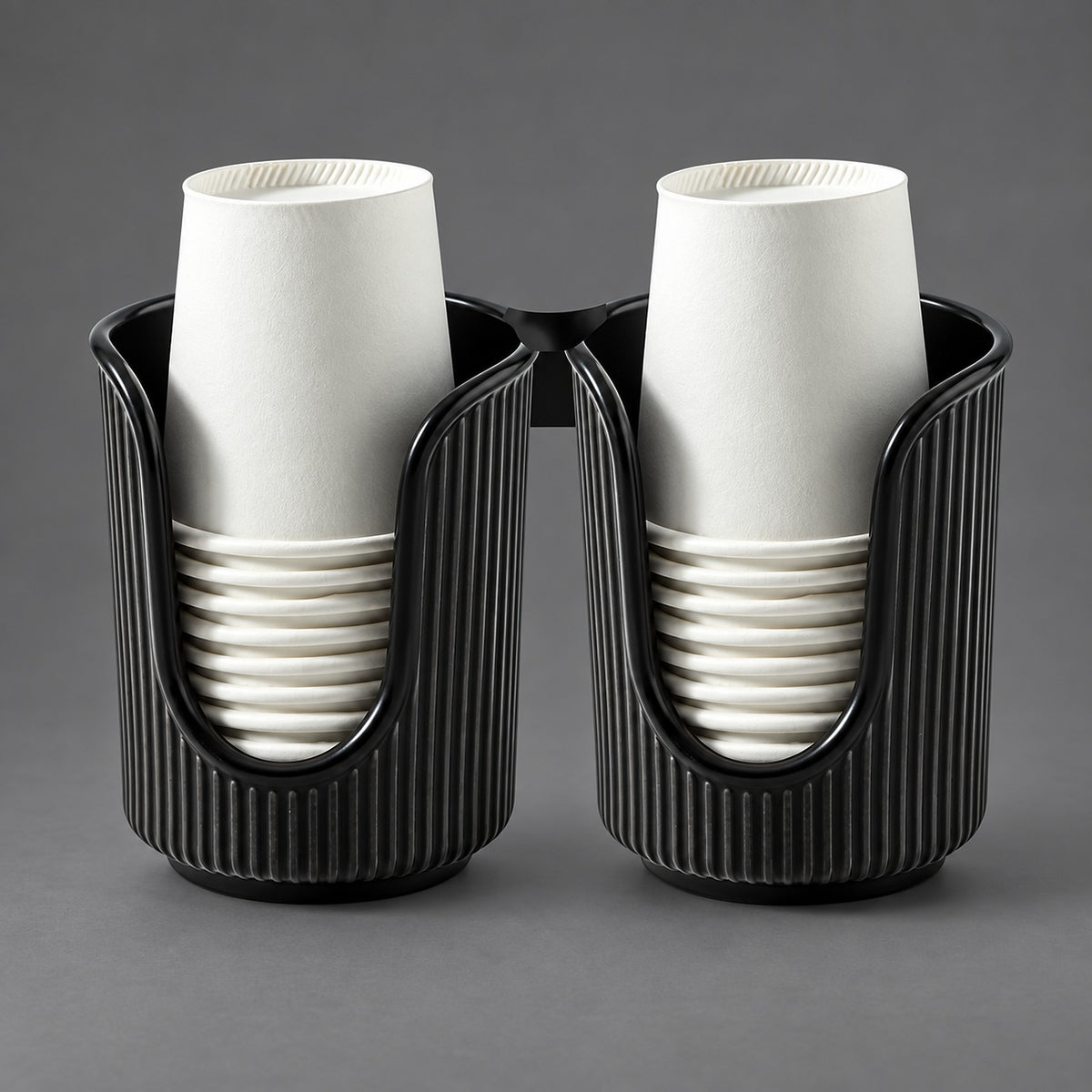 Two black ribbed cup holders, each holding a stack of white paper cups, photographed on a smooth gray studio background.