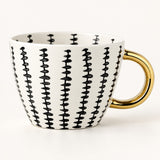 A white ceramic coffee mug with a black vertical dash pattern and a shiny gold handle, shown on a clean white background.