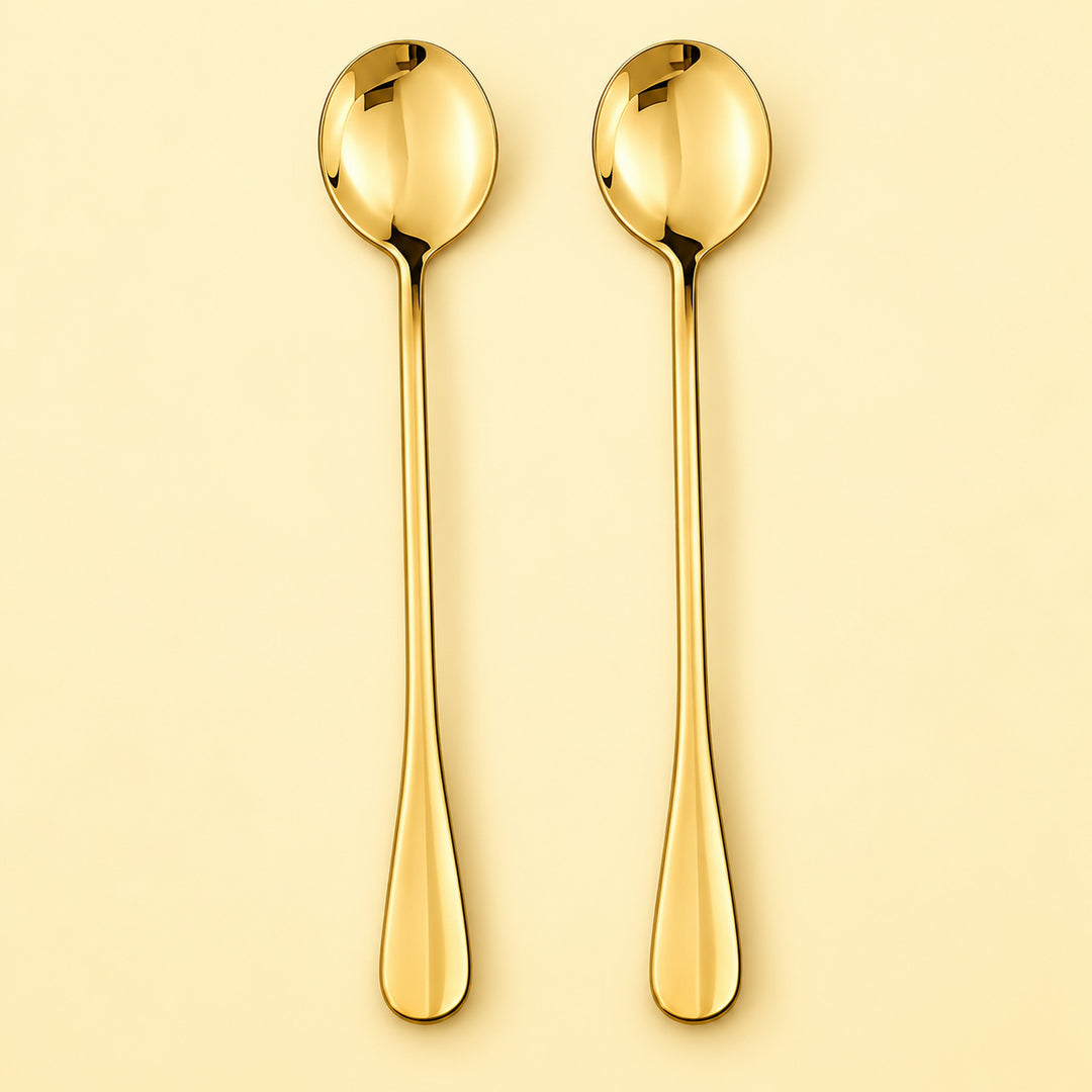 Two long gold spoons with oval bowls and tapered handles, shown upright on a warm cream background.