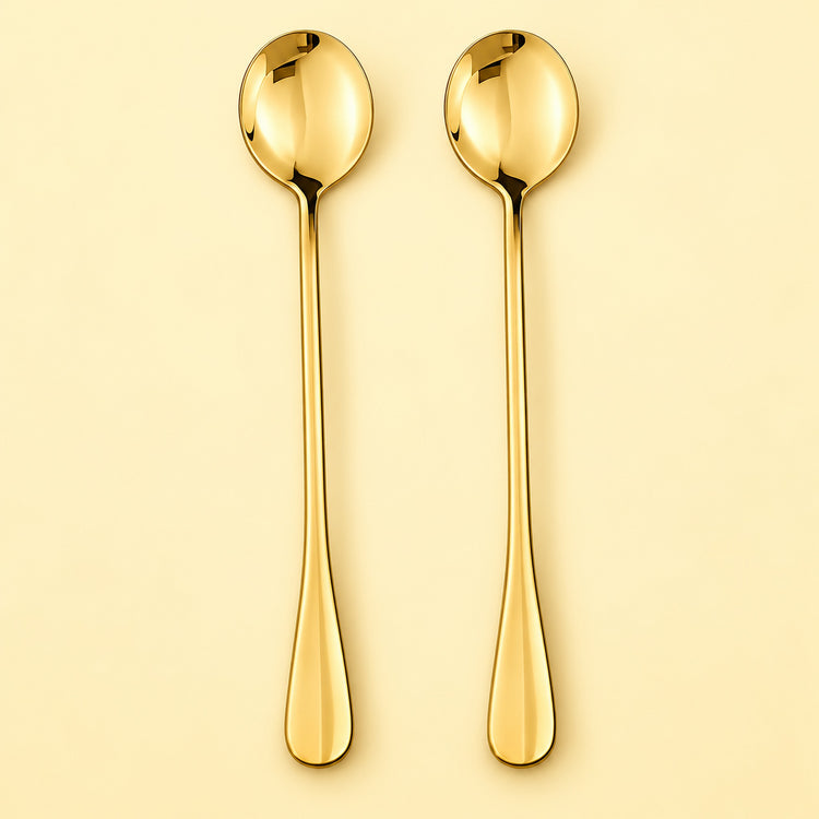 Two long gold spoons with oval bowls and tapered handles, shown upright on a warm cream background.